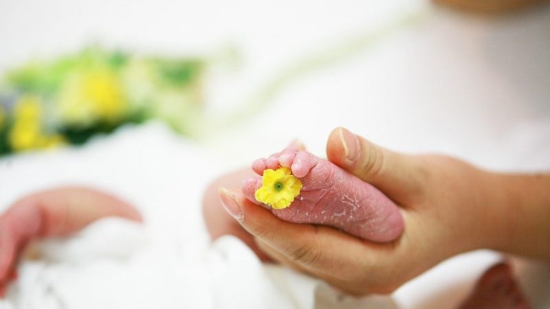 黄色い花のついた赤ちゃんの足を握る母親の手