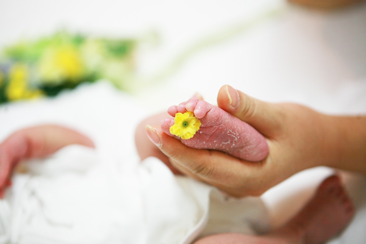 黄色い花のついた赤ちゃんの足を握る母親の手
