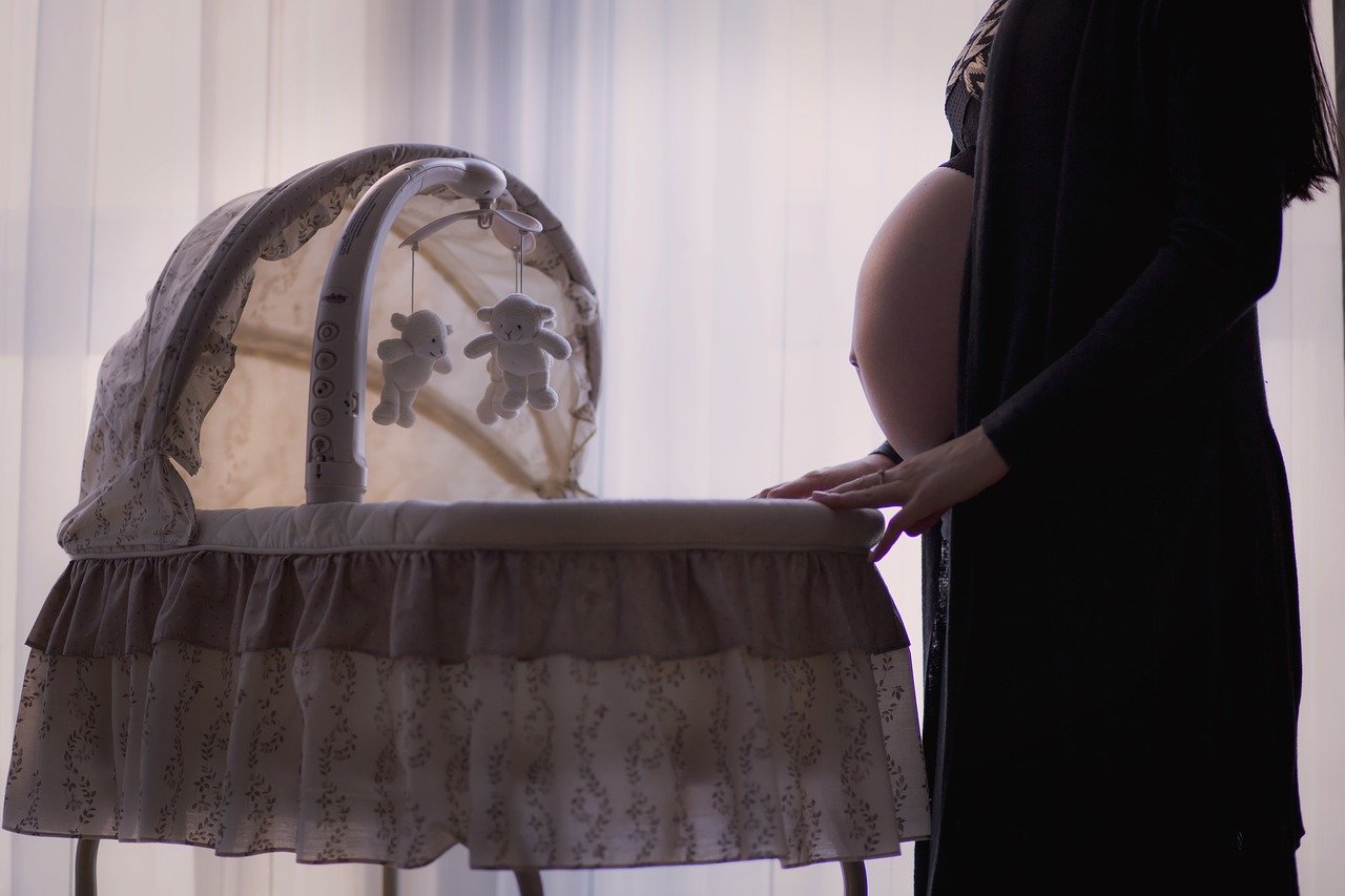 赤ちゃん用のベッドに手を添える妊娠中の女性