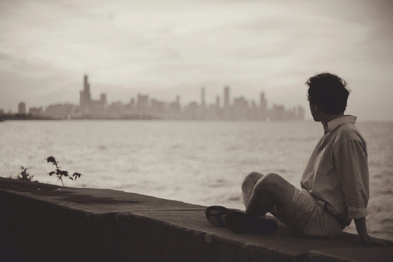 海辺に座って対岸の都市を見つめる男性のセピア写真